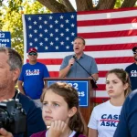 Casey Askar speaking at a political rally, supporters holding signs for FL-22.